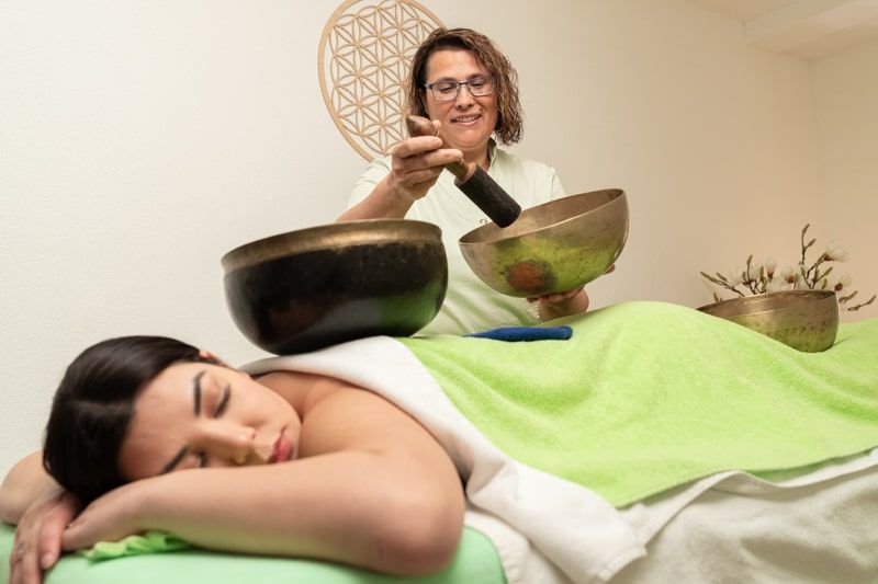 Infobild Klangmassage: Klangschale mit liegender, entspannter Frau im Hintergrund